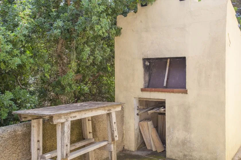 Una zona de trabajo al aire libre con una mesa de madera junto a una pequeña estructura de yeso.