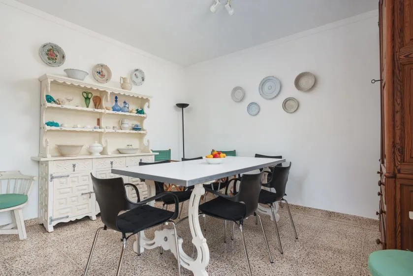 Comedor con una mesa grande, asientos oscuros y vajilla expuesta en estantes.