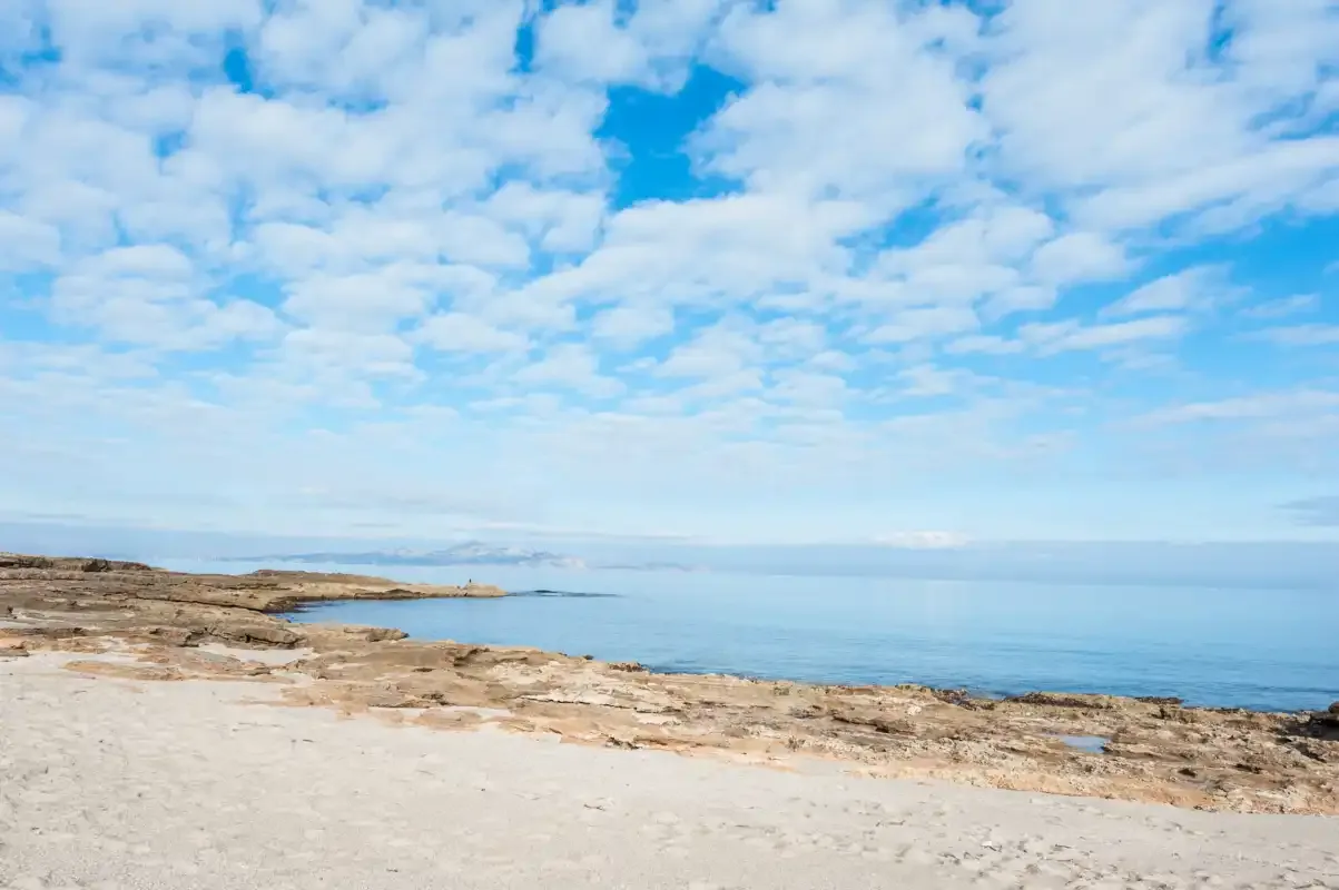 Una costa rocosa se encuentra con aguas tranquilas bajo un cielo nublado.
