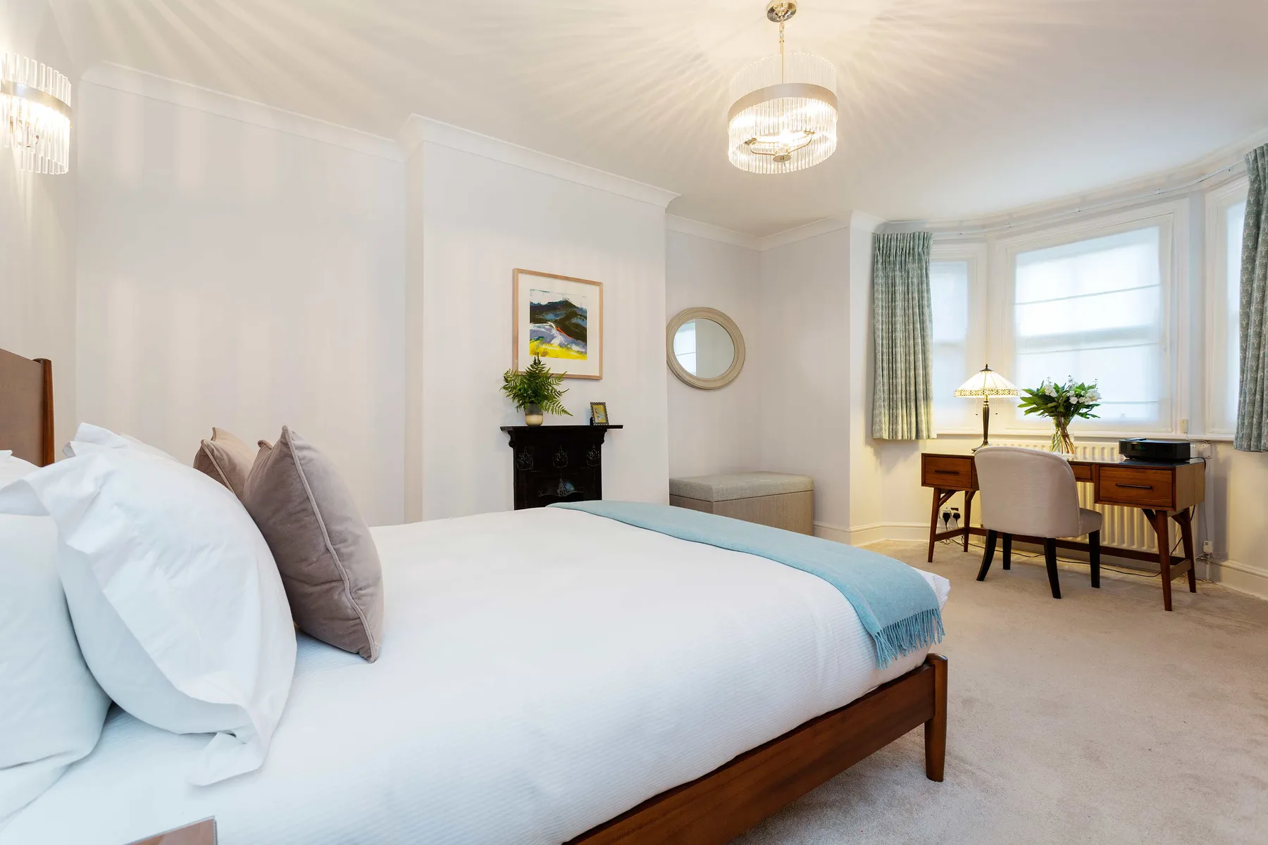 A bright bedroom with a large bed and a desk beside the bay window.