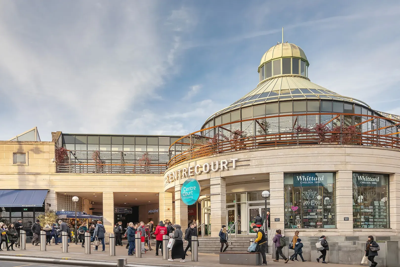 A shopping center with a glass-domed upper level and pedestrians outside.