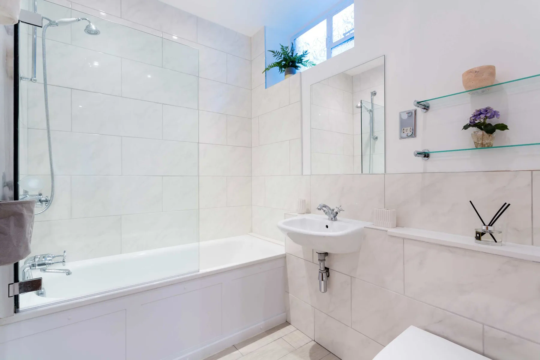 A bright tiled bathroom with a bathtub, sink, and wall mirror.