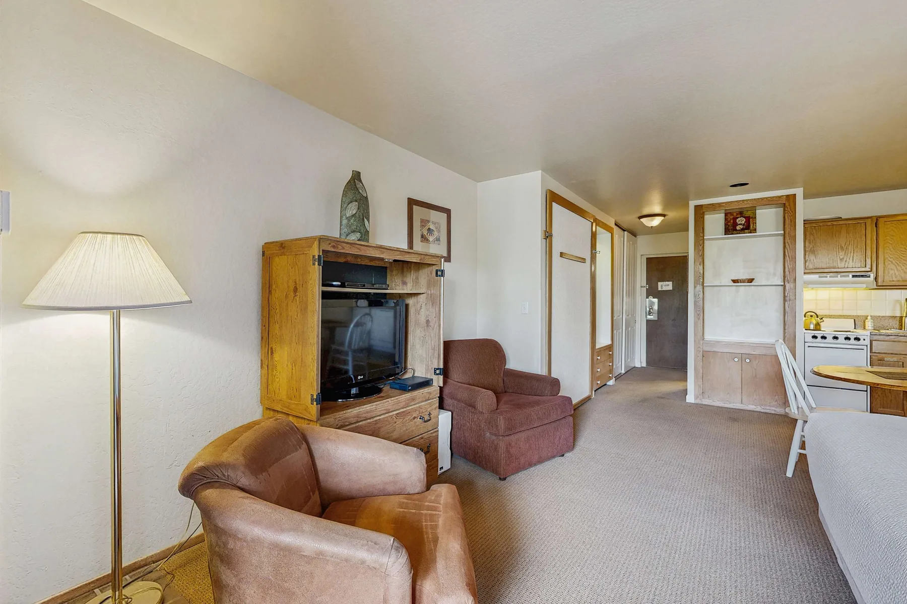 Una sala de estar con asientos, un mueble para televisión y una lámpara de pie.