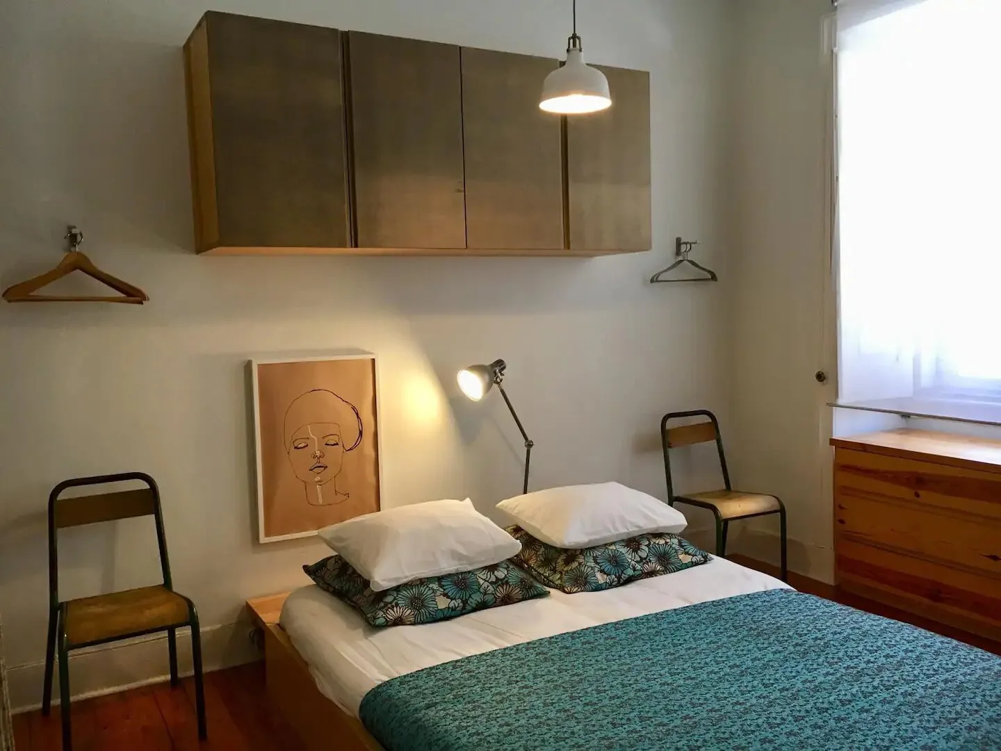 Un dormitorio con una cama baja, ropa de cama color turquesa y armarios en la pared.