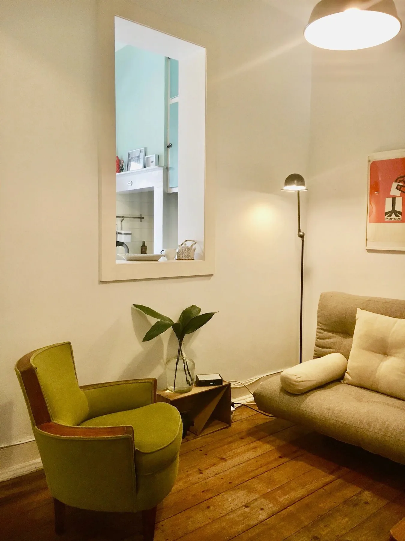 Una sala de estar con asientos verdes, un sofá beige y una lámpara de pie.