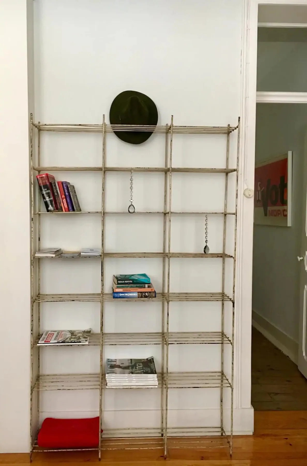 Una estantería metálica con algunos libros está junto a una puerta, contra una pared blanca.