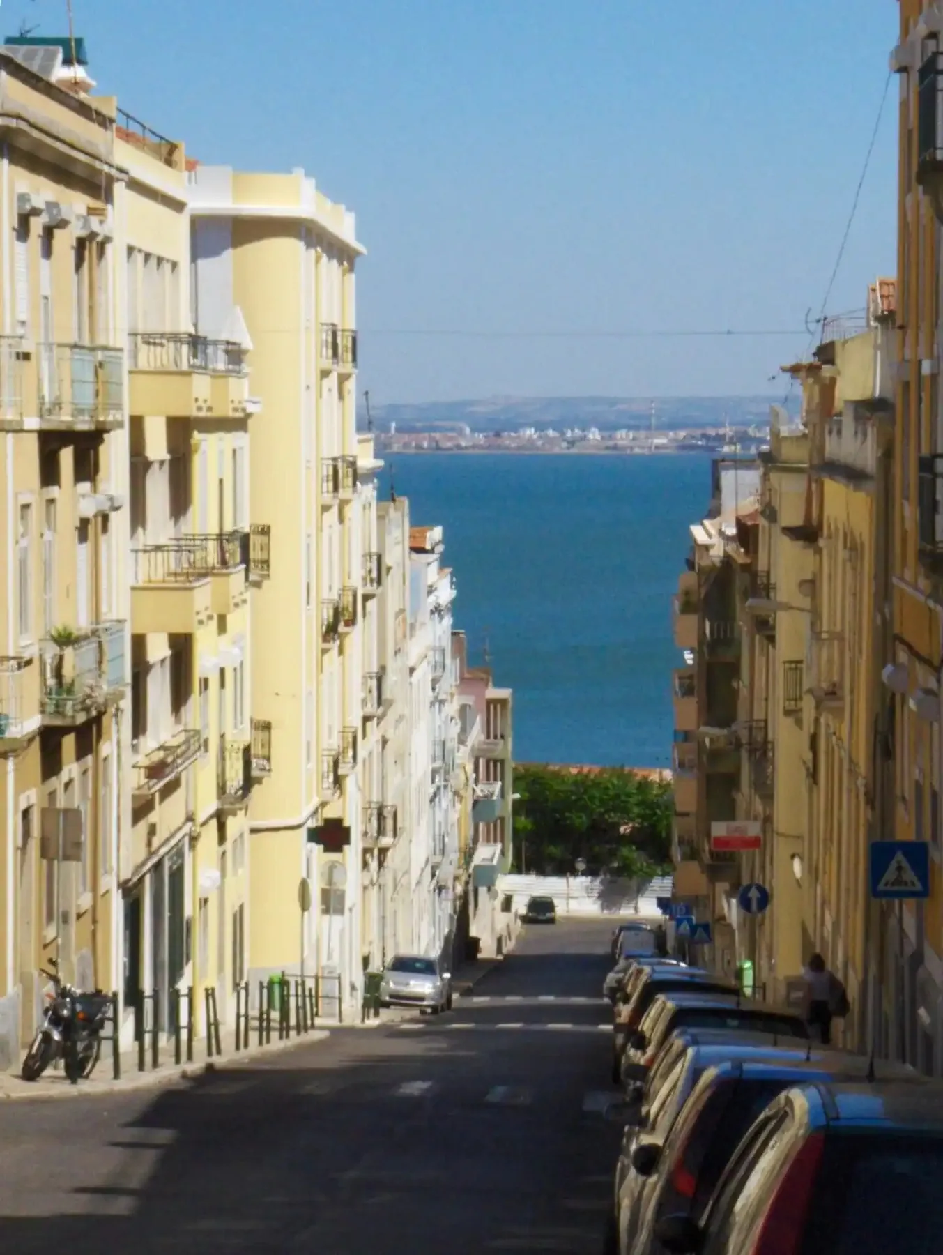 Una calle urbana en pendiente, flanqueada por edificios, conduce hacia una vista del agua.