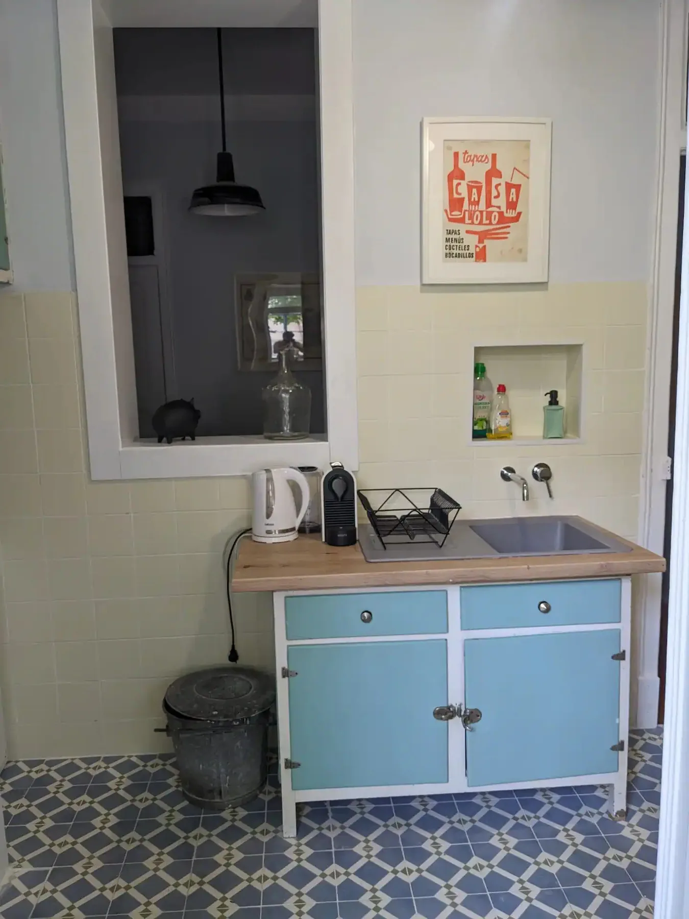 Una cocina compacta con un mueble azul, fregadero y suelo de baldosas.
