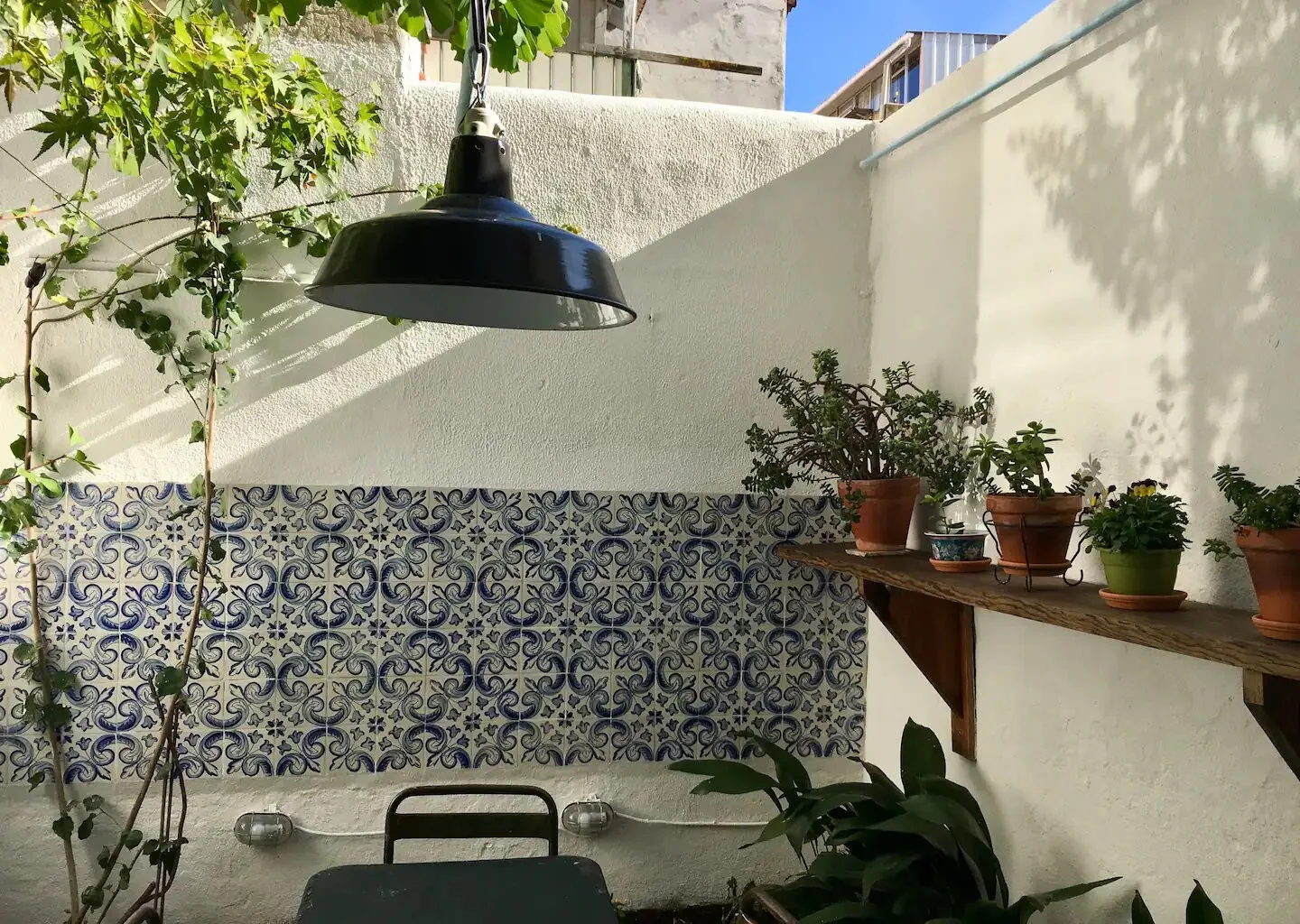 Un pequeño patio con paredes de azulejos estampados, plantas en macetas y una mesa.