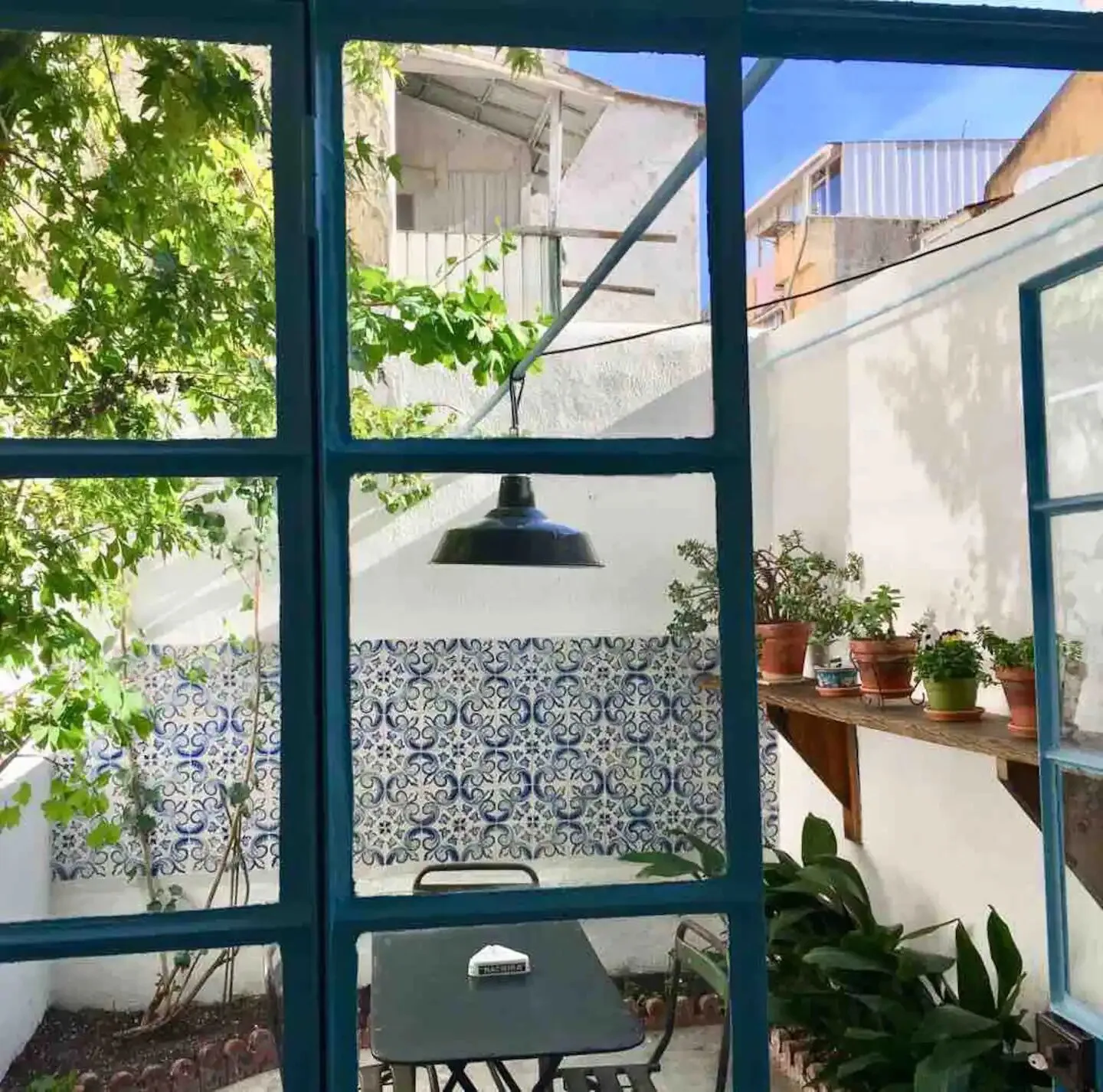 Un jardín de patio se ve a través de puertas de vidrio con marco oscuro, con paredes de azulejos estampados y plantas en macetas.
