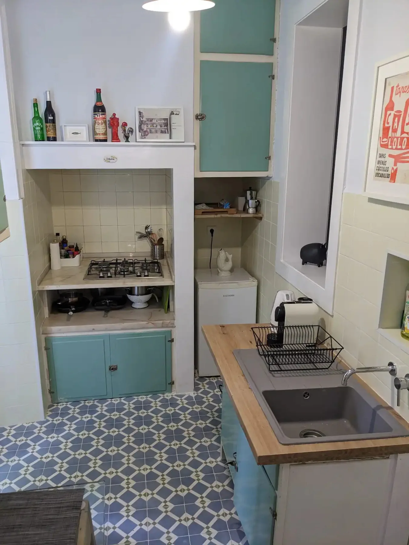 Una cocina compacta con cocina de gas, fregadero y suelo de baldosas estampadas.