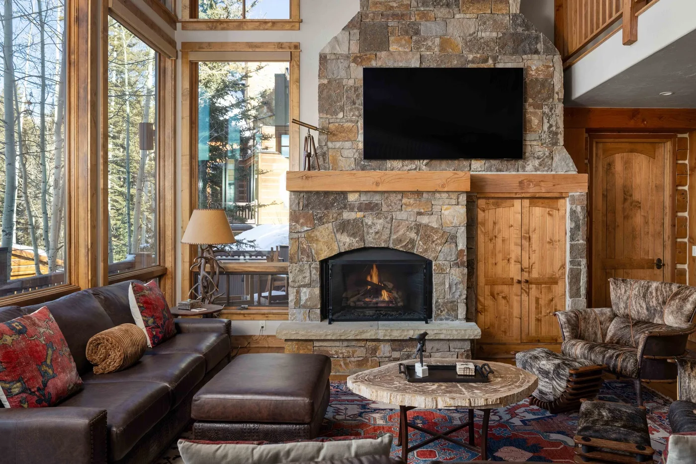 A living room with a stone fireplace, large windows, and seating around a coffee table.
