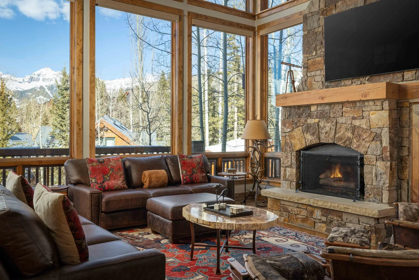 A living room with seating beside a stone fireplace and large windows.