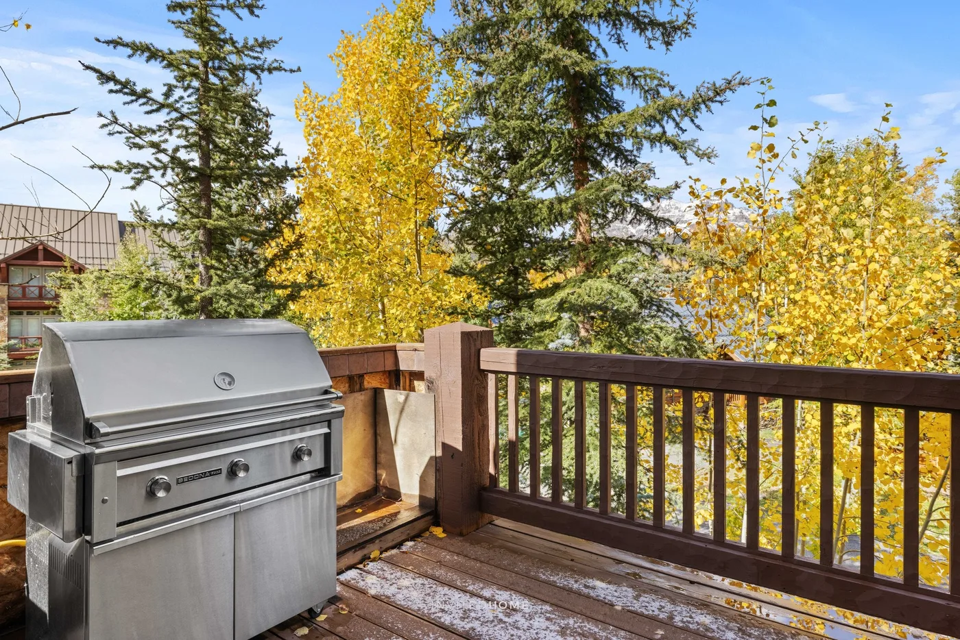 A wooden deck with a stainless steel grill overlooks colorful autumn trees.