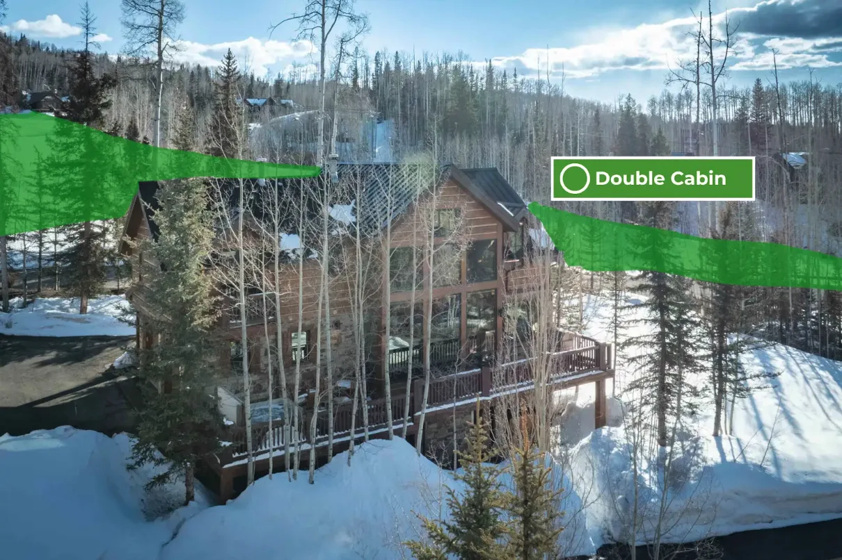 A wooden cabin with large windows stands among snow-covered trees.