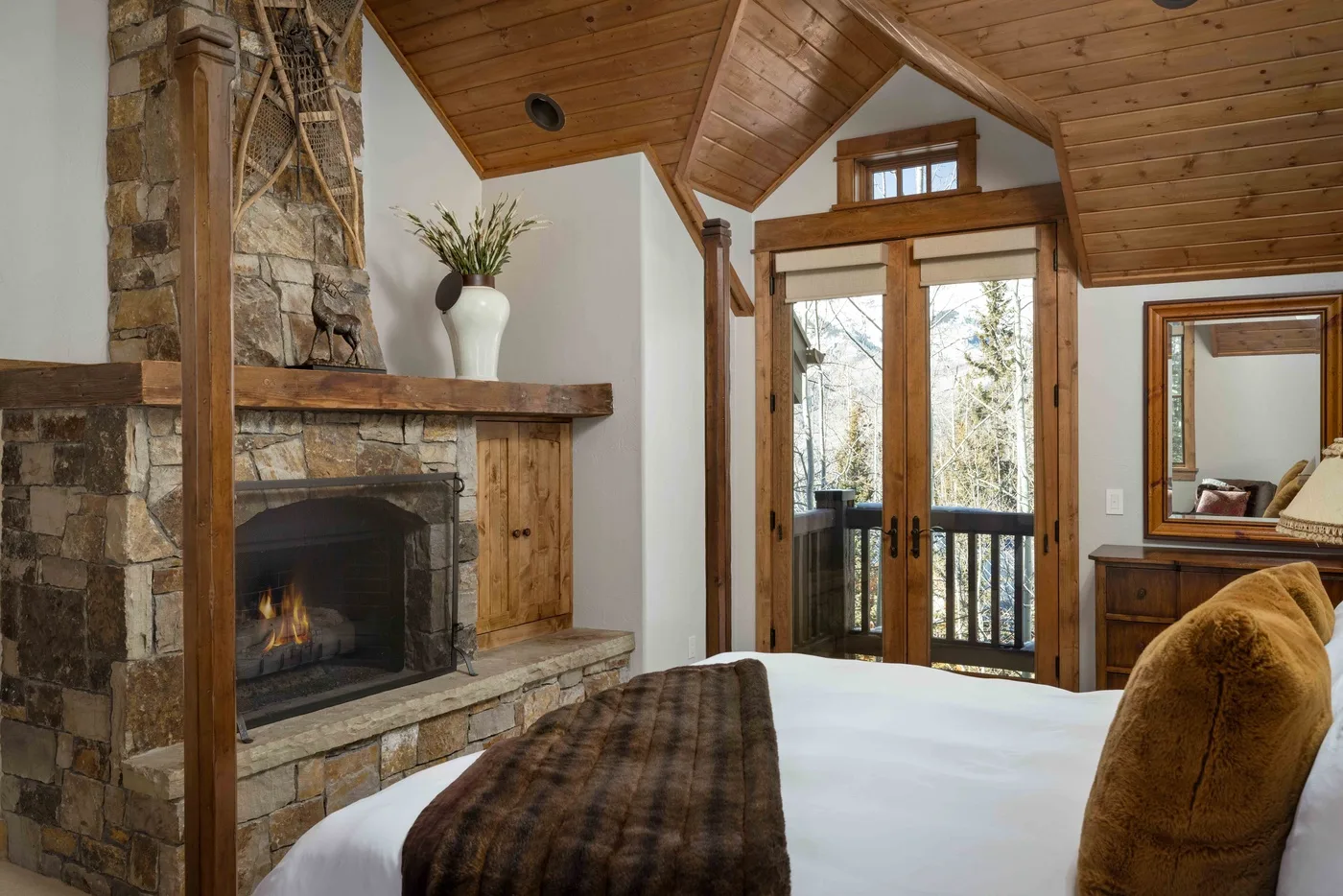 A bedroom with a stone fireplace and glass doors opening onto a balcony.