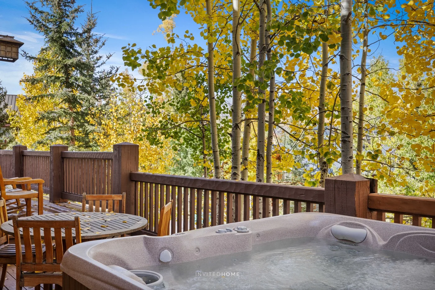A deck with a hot tub and outdoor dining table overlooks leafy trees.