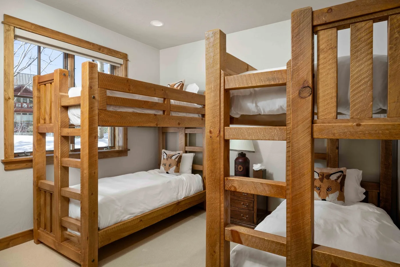 A bedroom with wooden bunk beds, white bedding, and a large window.
