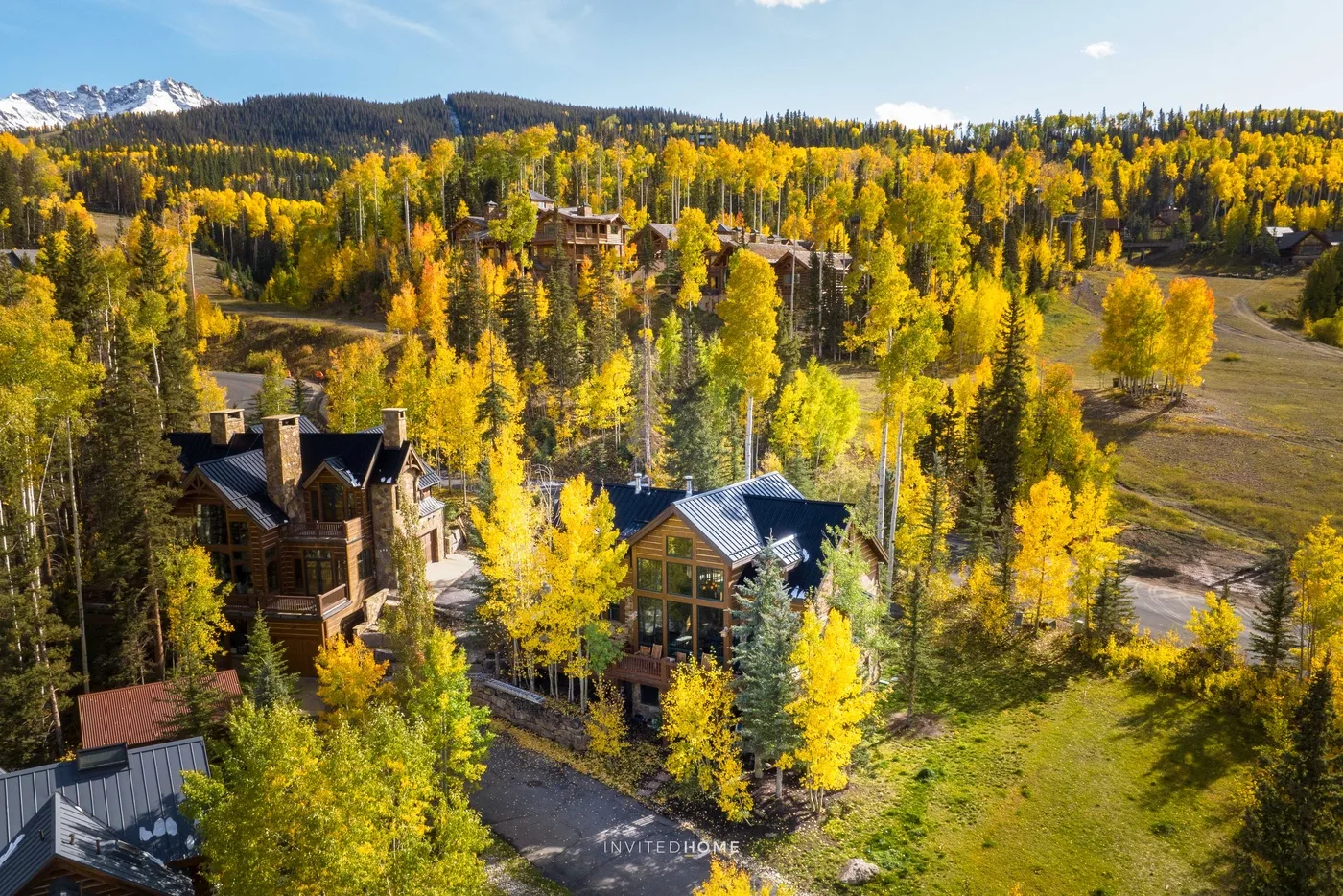 Cabins sit among golden autumn trees, with forested hills and mountains in the distance.