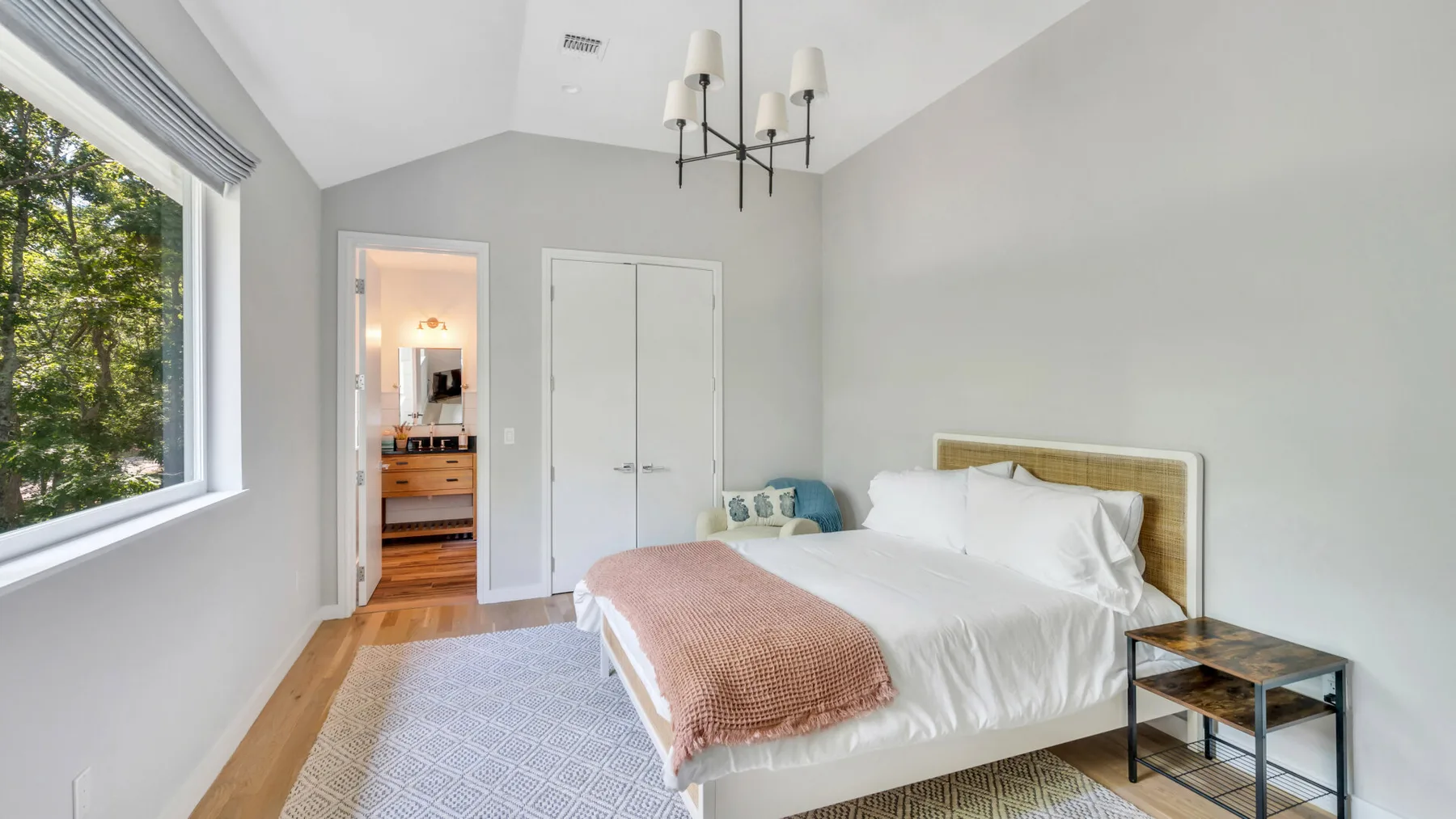 A bright bedroom with a large bed and a window overlooking trees.