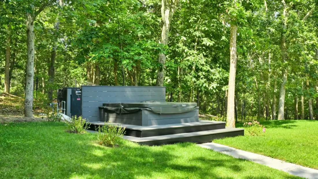 An outdoor hot tub sits on a raised platform in a wooded garden.