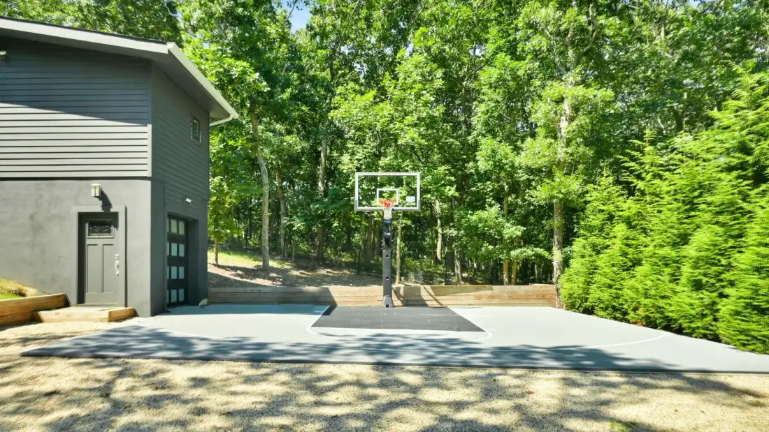 An outdoor basketball court sits beside a building, surrounded by trees.