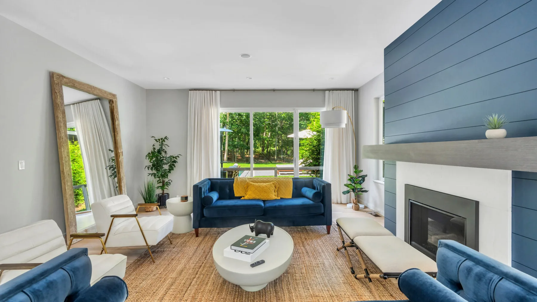 A bright living room with blue seating, a round coffee table, and a fireplace.