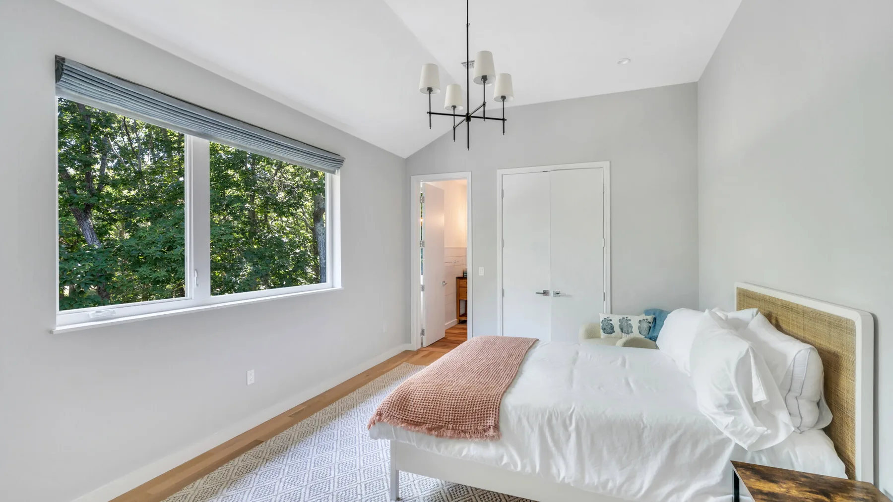 A bright bedroom with a large window and a neatly made bed.