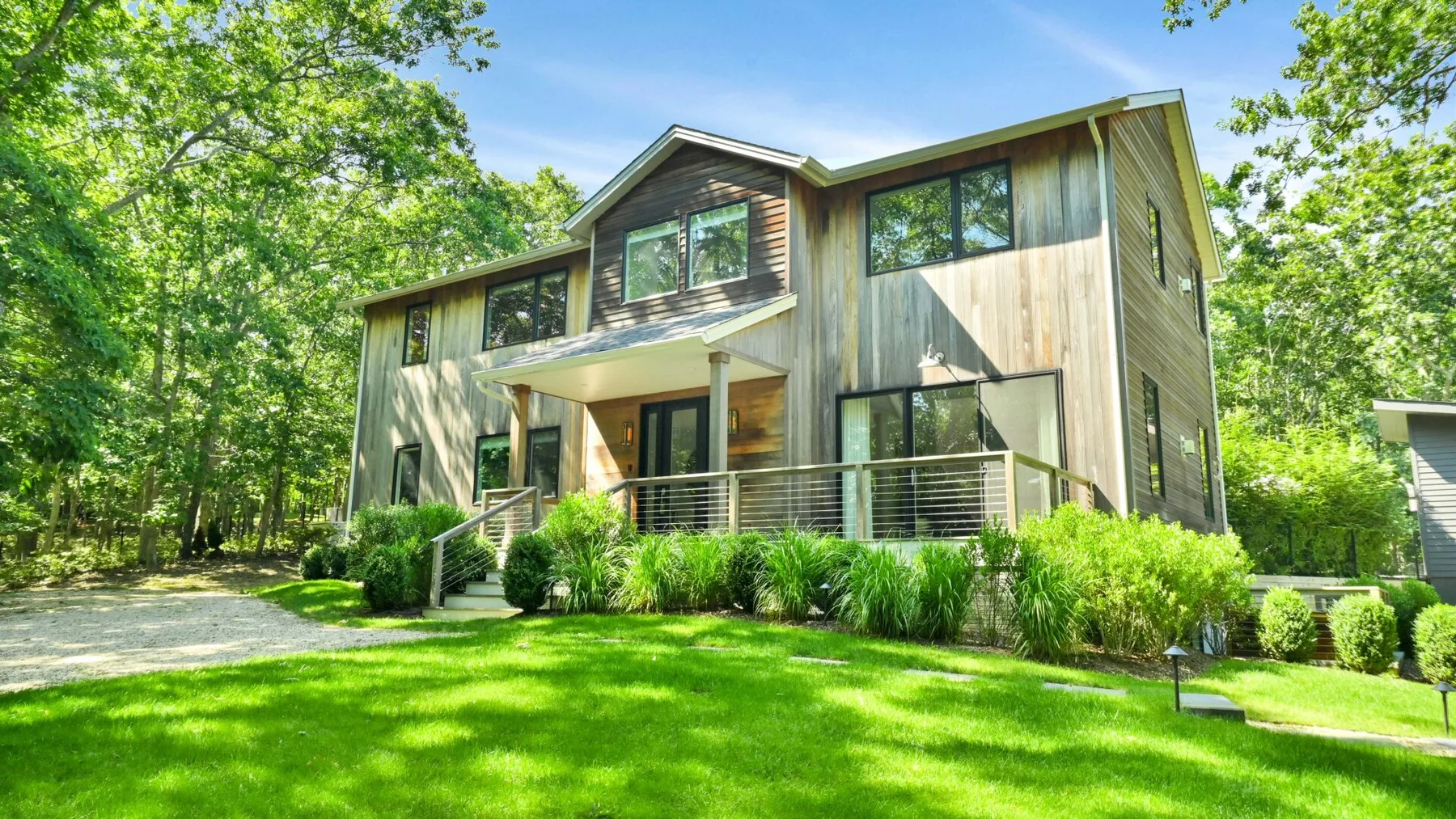 A modern two-story house stands beside a green lawn and leafy trees.