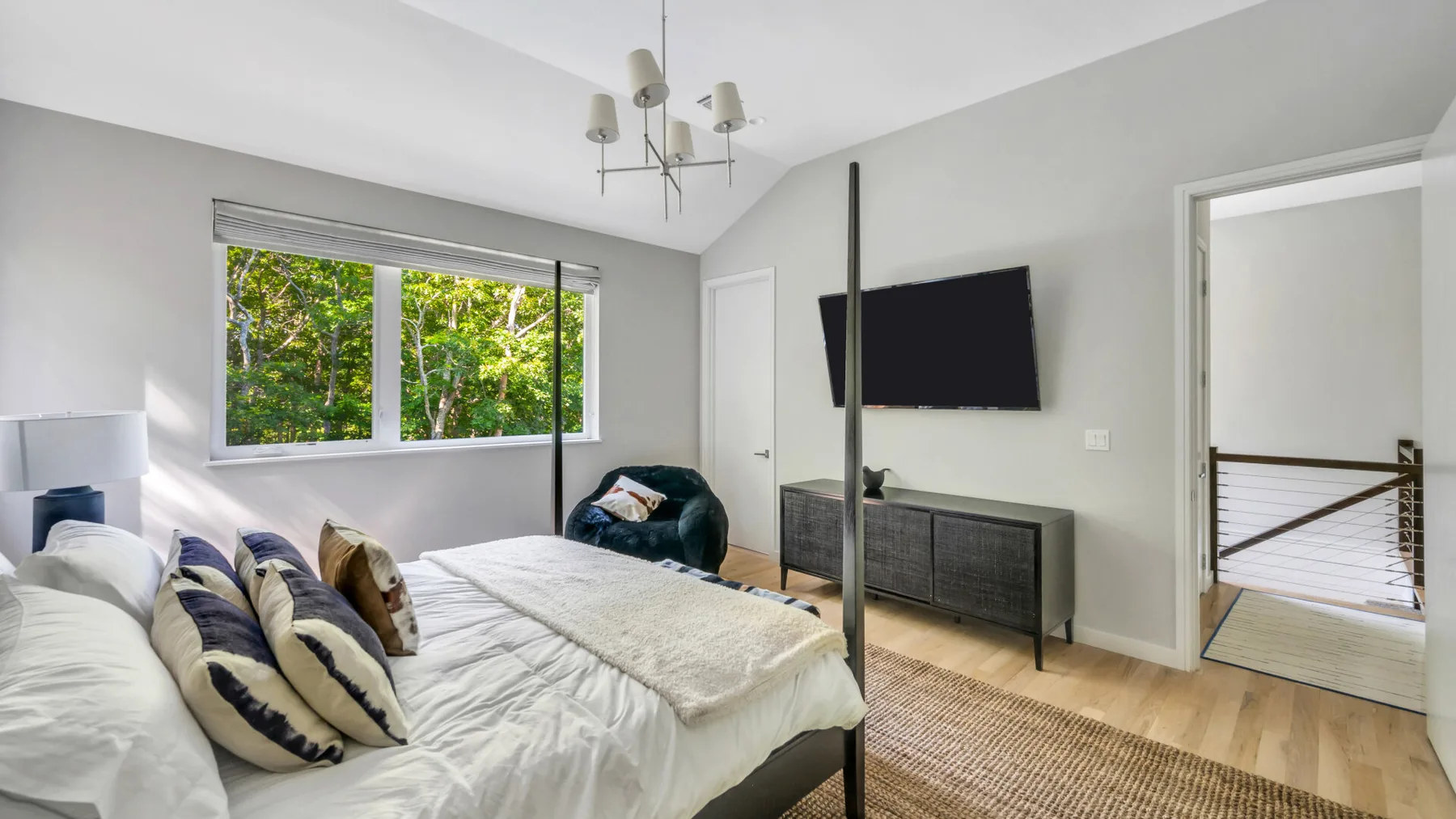 A bright bedroom with a large bed, television, and windows overlooking greenery.