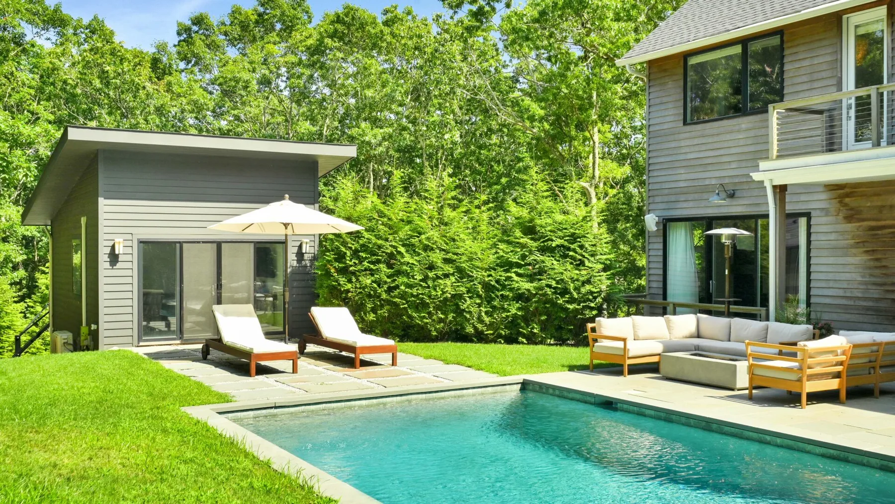 A backyard pool sits beside a patio with outdoor seating and a small outbuilding.