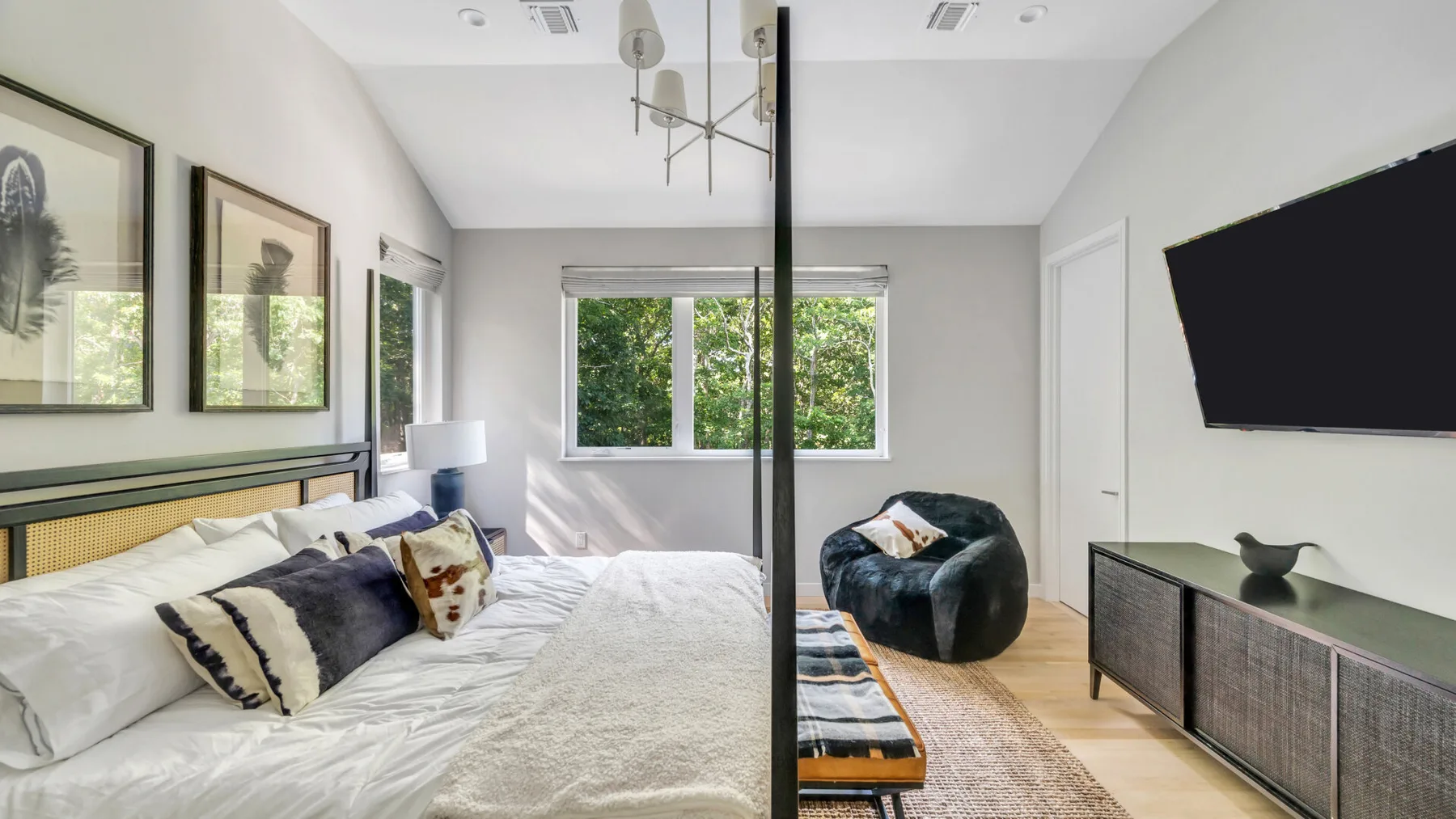 A bright bedroom with a bed, large window, and television.