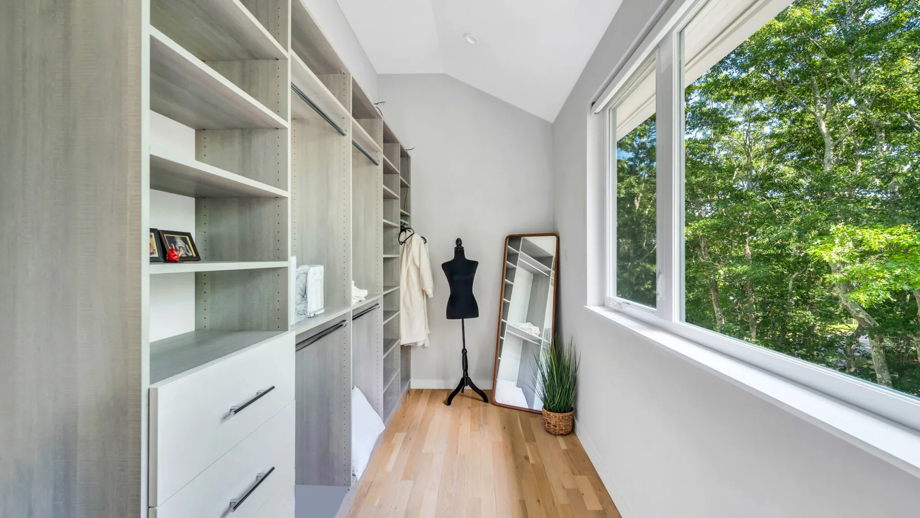A bright dressing room with open shelving, a full-length mirror, and large windows.