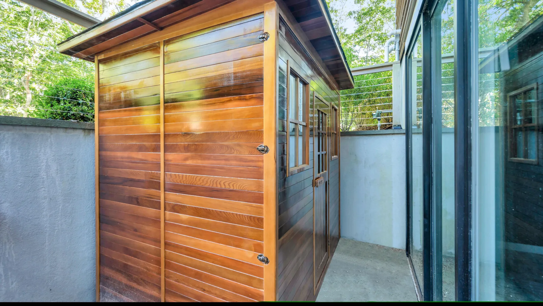 A wooden shed stands beside a glass-walled outdoor walkway.