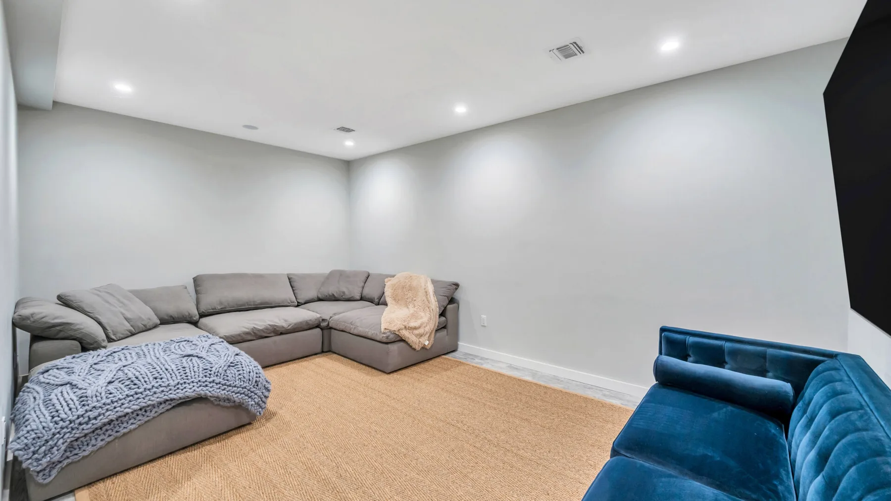 A living room with gray seating and a blue armchair around an open rug.
