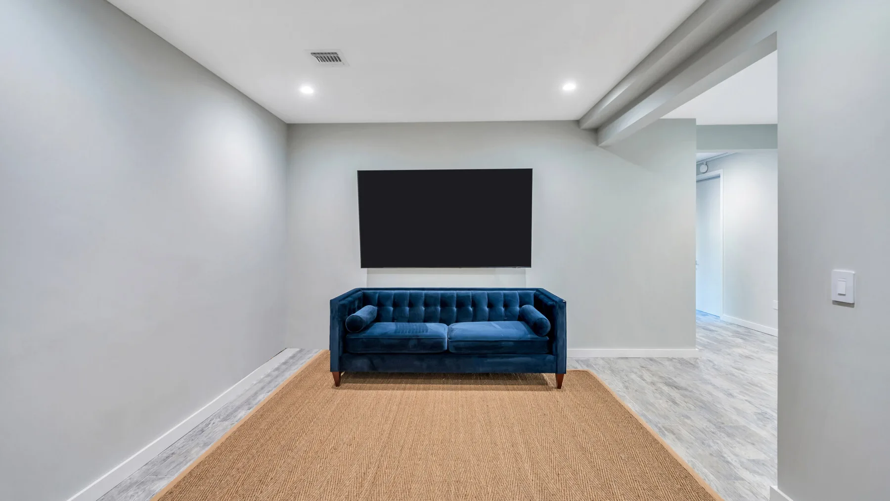 A living room with a blue sofa, wall-mounted television, and large rug.