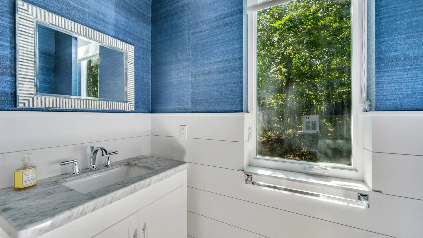 A bathroom vanity with a wide mirror sits beside a large window.