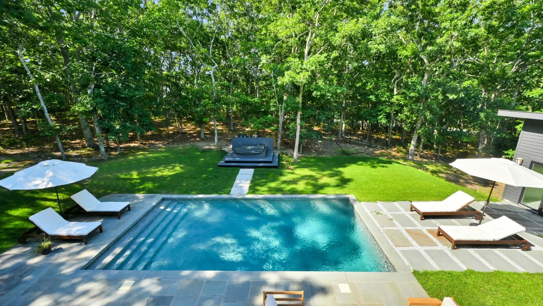 Una piscina exterior junto a una zona de descanso pavimentada y un césped verde.