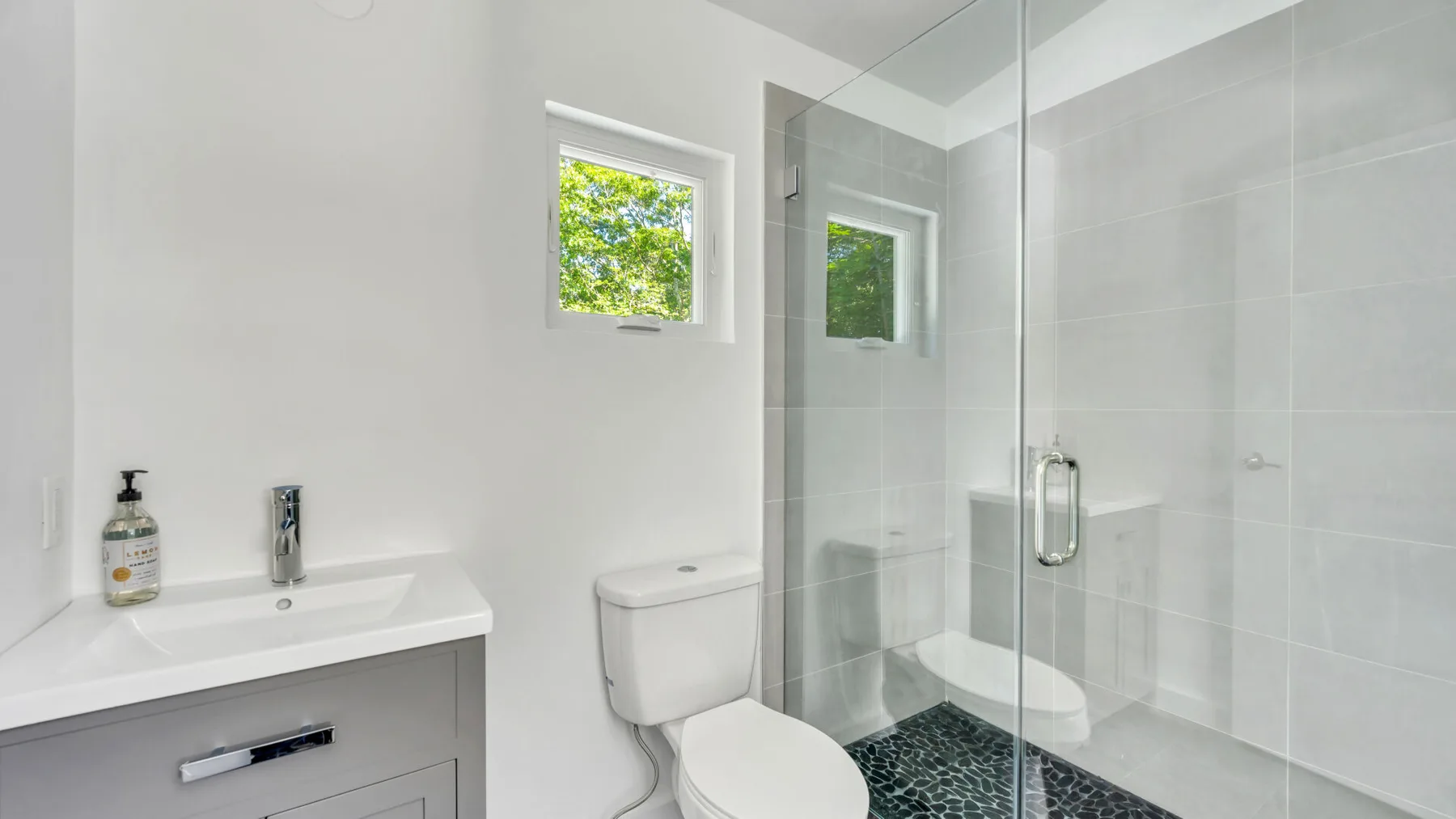 A bright bathroom with a vanity, toilet, and glass-enclosed shower.