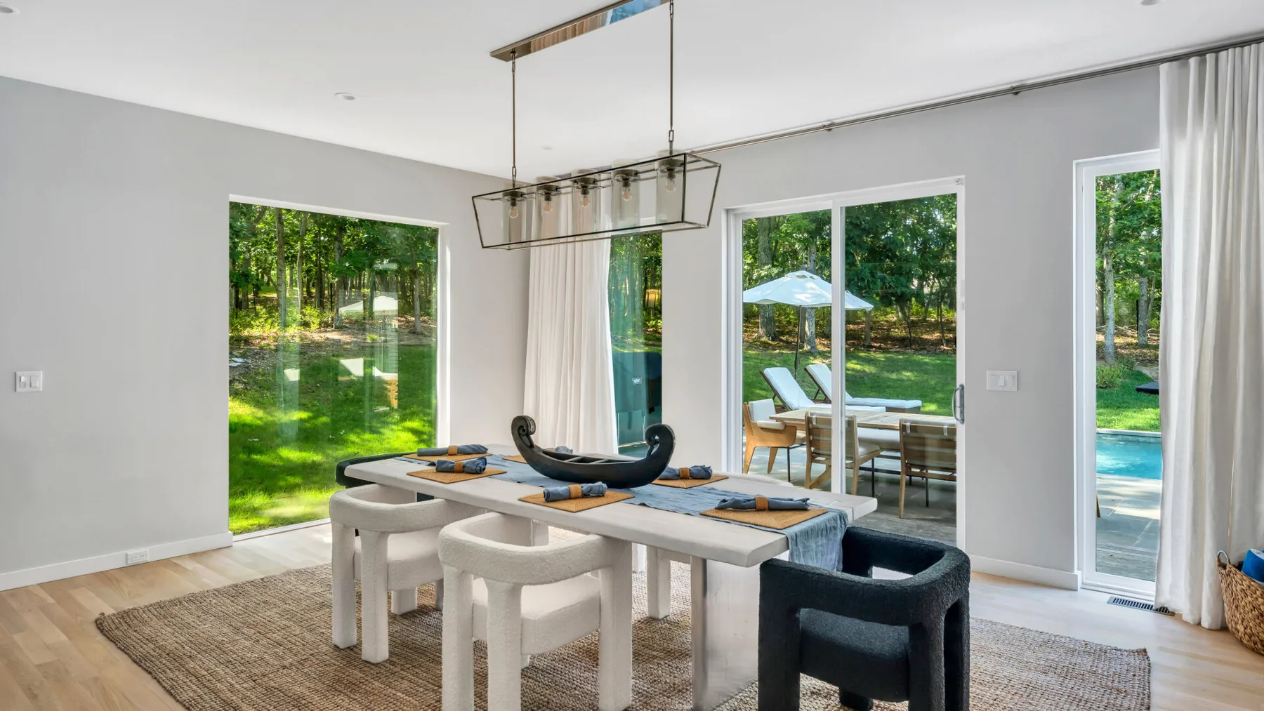 A bright dining area with a long table and large windows overlooking greenery.