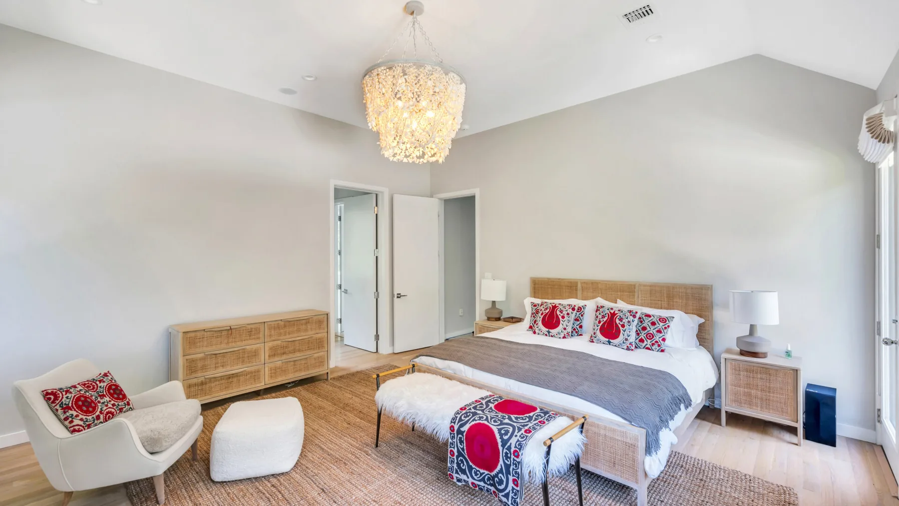 A bright bedroom with a bed, bedside tables, and a chandelier.