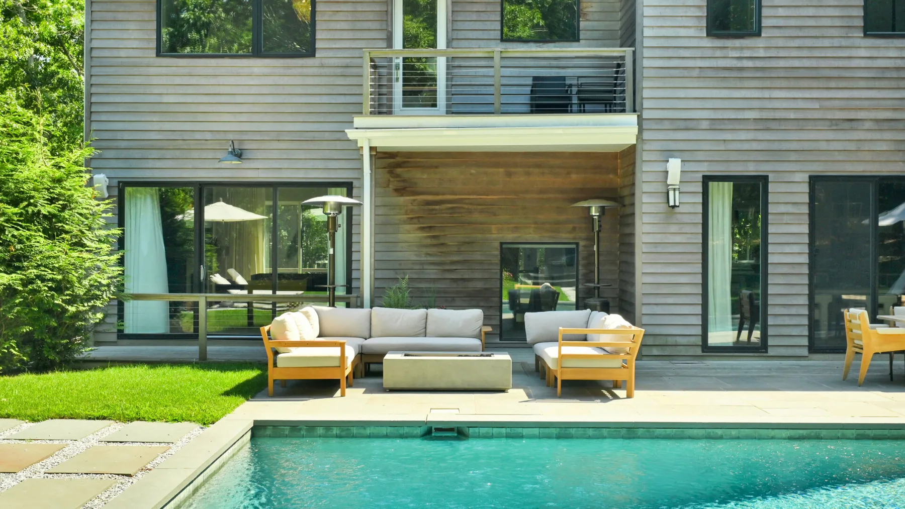 A swimming pool beside a patio with outdoor seating and a modern house.