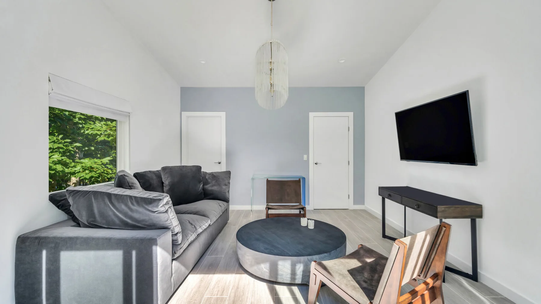 A living room with gray seating, a round coffee table, and a wall-mounted television.