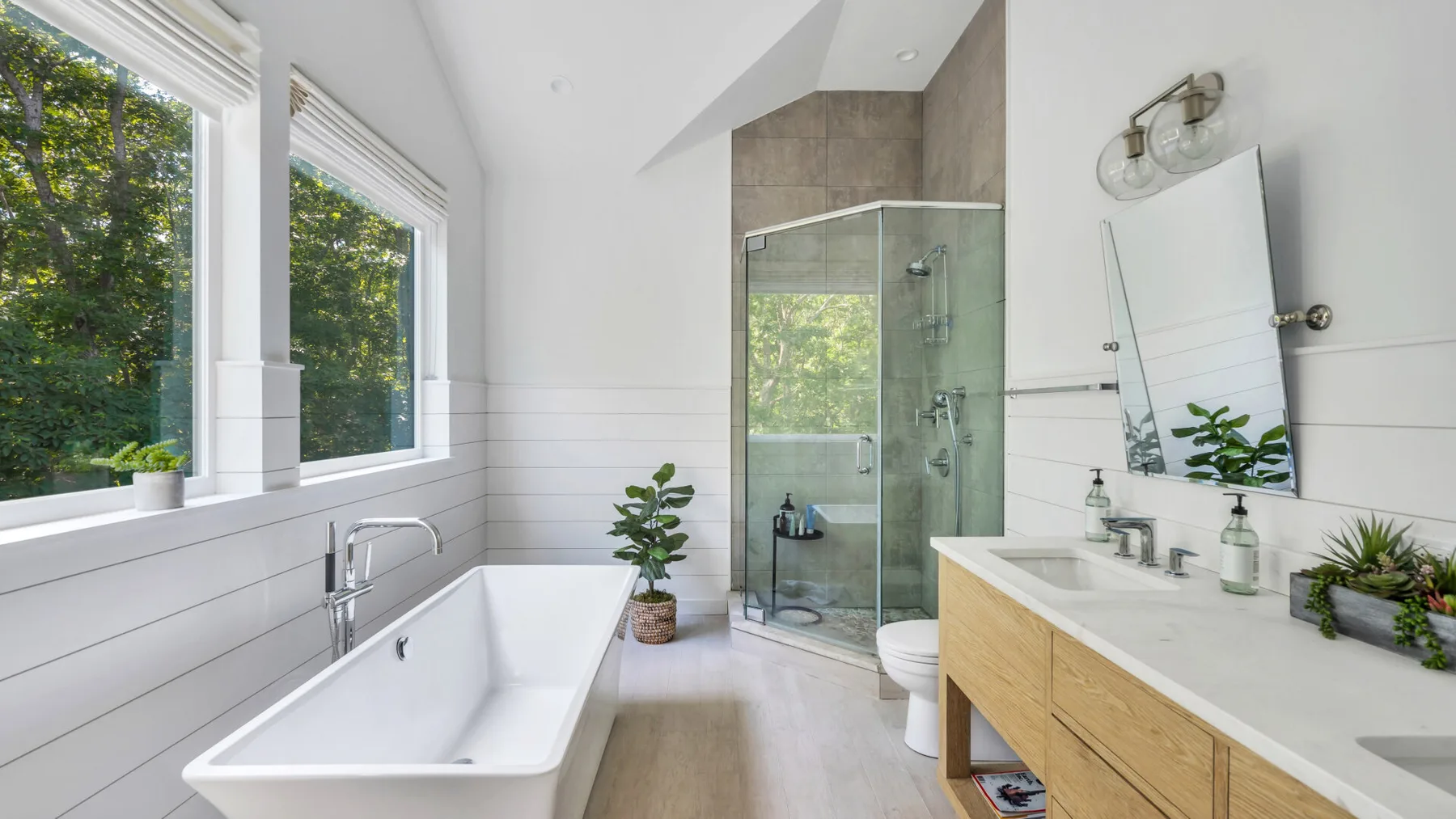 A bright bathroom has a freestanding tub, glass shower, and wide windows.
