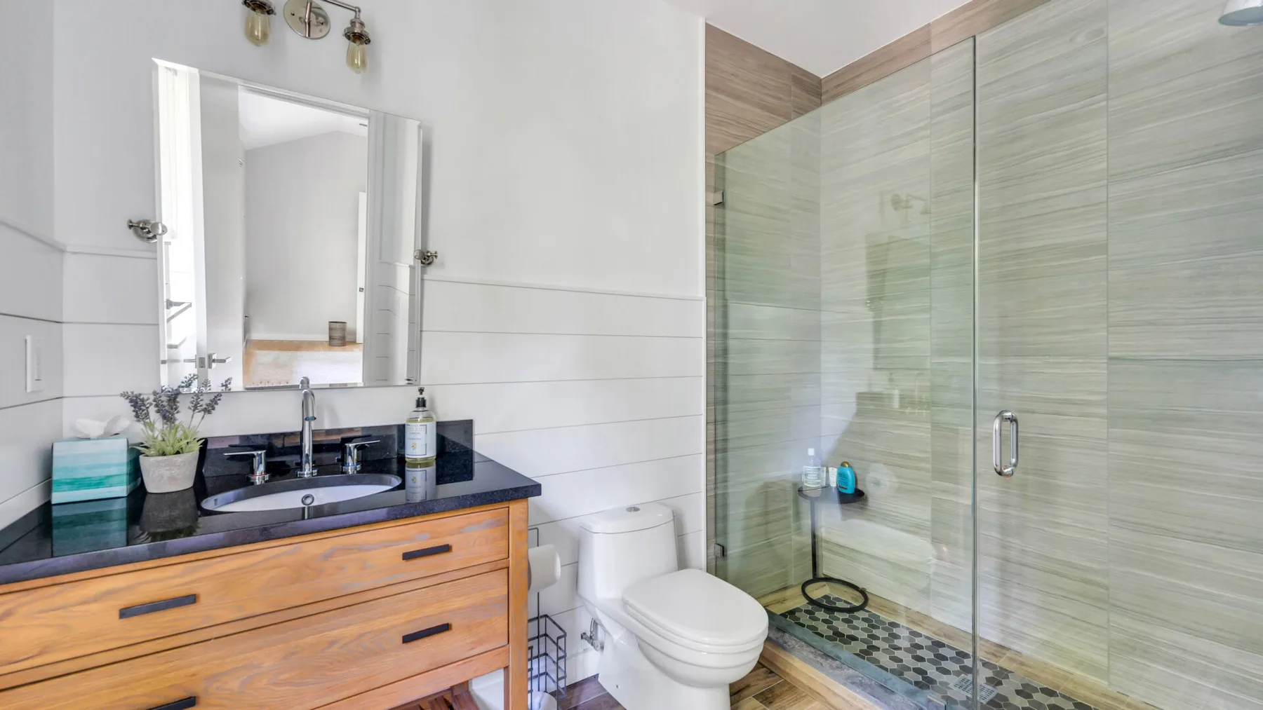 A bathroom with a wood vanity, sink, toilet, and glass shower.