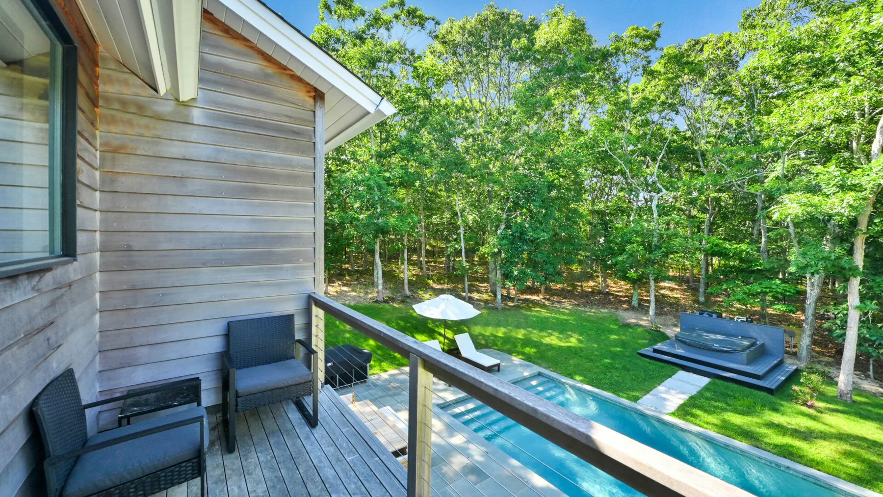 A deck overlooks a green yard with trees and an outdoor hot tub.
