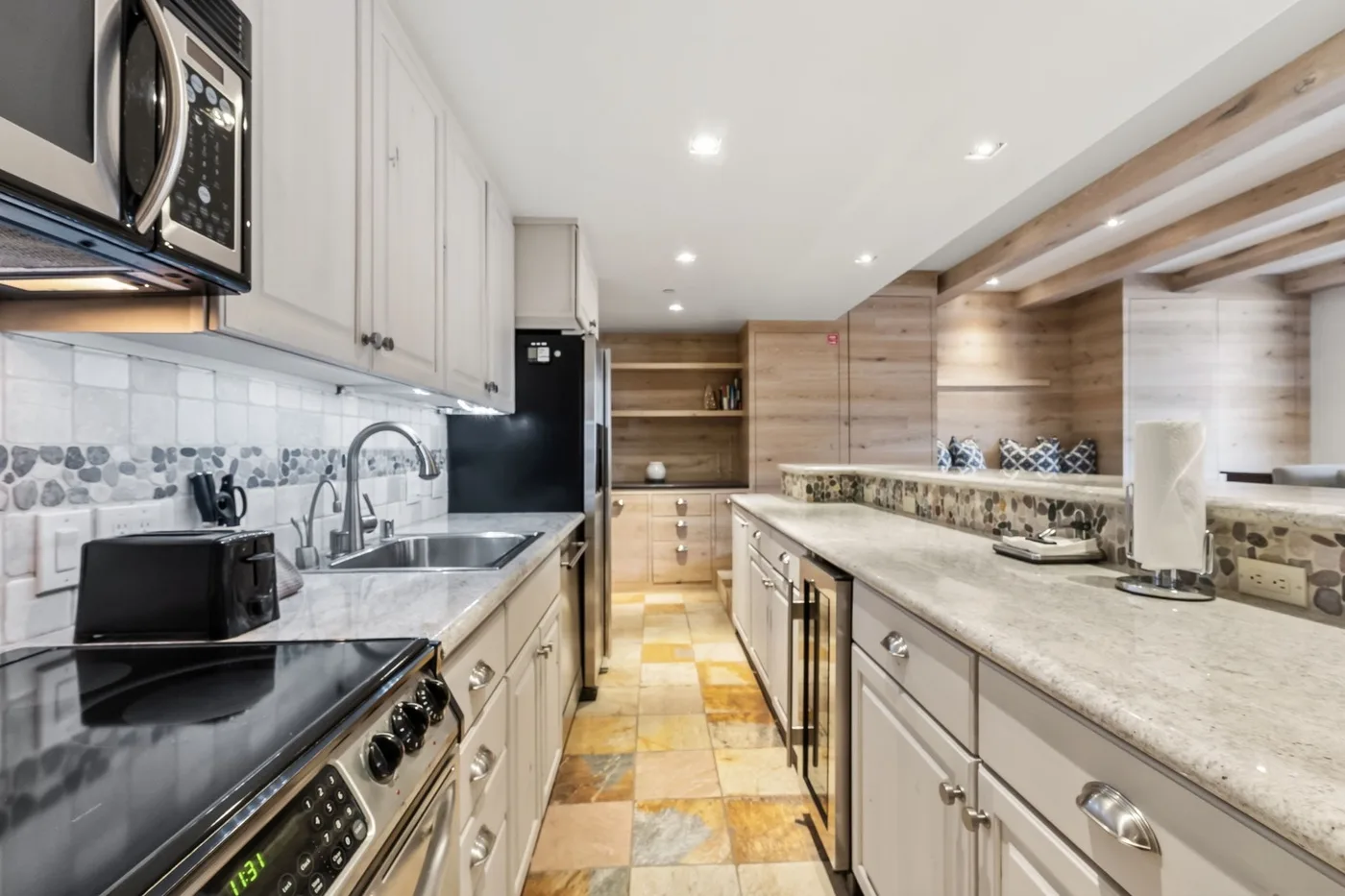 Una cocina luminosa con largas encimeras, gabinetes claros y electrodomésticos de acero inoxidable.