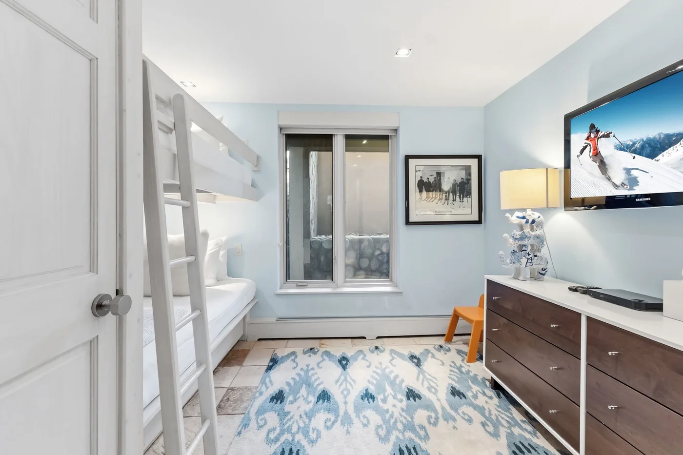 Un dormitorio azul claro con literas, una ventana y una alfombra estampada.