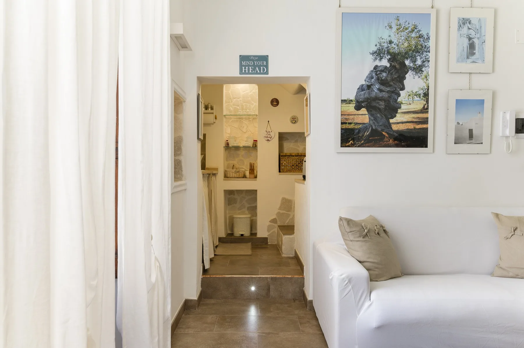 A bright living area with white seating and a view into a bathroom.