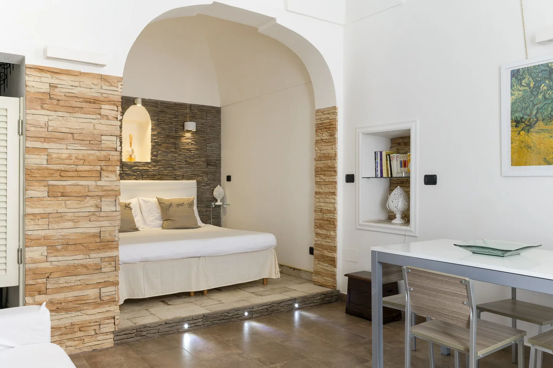 A bedroom with a bed beneath an arched opening and a desk nearby.